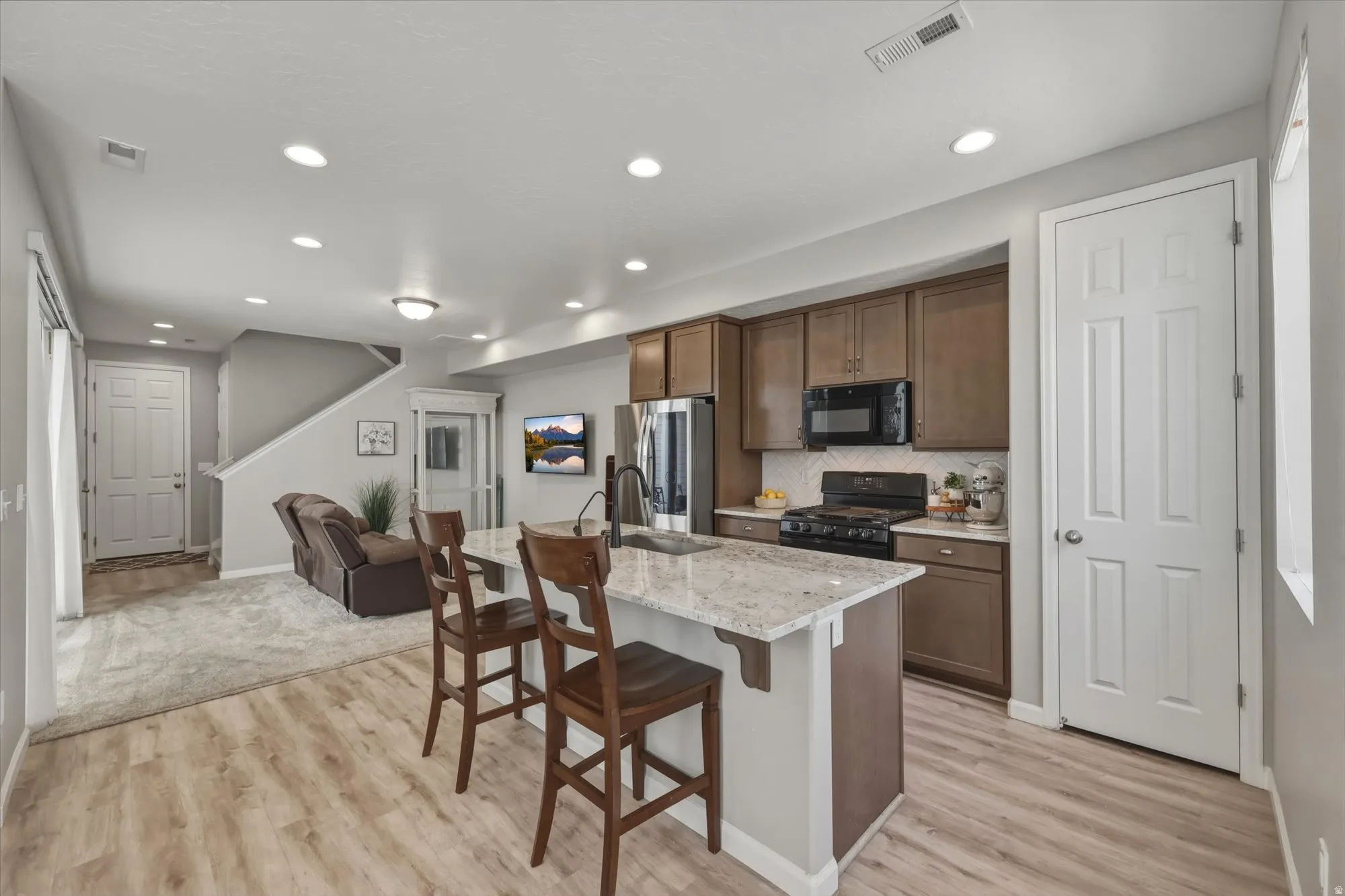 Kitchen featuring light-tone wood-finish flooring, a white granite-style island with seating, dark wood cabinetry, and a black appliance suite including a gas range