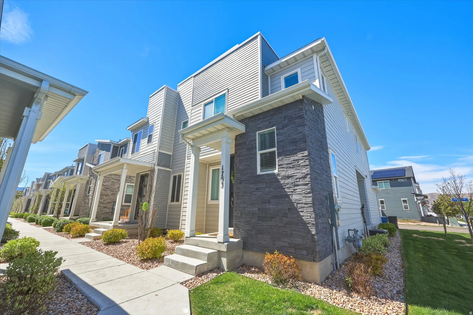 Modern townhome exterior featuring light-colored siding and a contrasting dark stacked stone facade