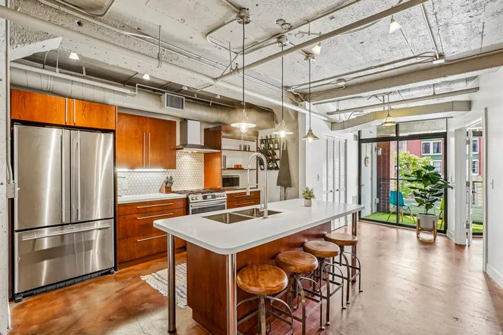 Modern kitchen featuring stainless steel appliances, wood cabinetry, and a white countertop island with an integrated sink