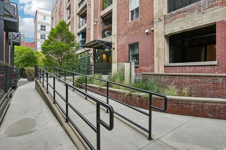 Exterior concrete ramp with black metal railings, bordered by a brick facade building with concrete accents
