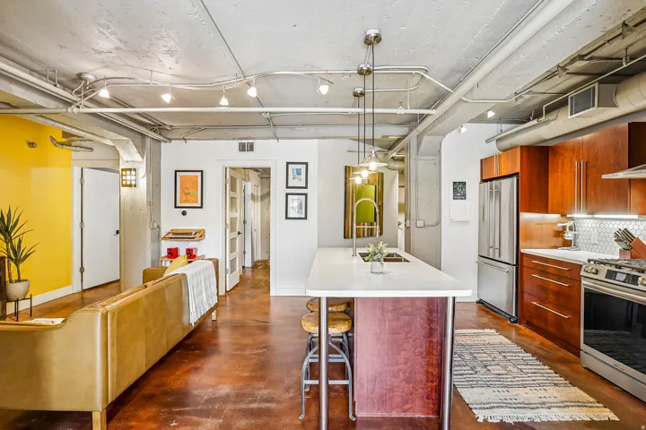 Open-concept living space featuring a central kitchen island with seating, stainless steel appliances, wood-finish cabinetry, and exposed ceiling elements
