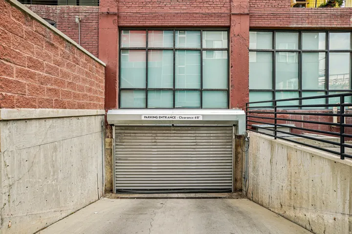 Dedicated parking entrance featuring a roll-up security door, a concrete ramp, and concrete retaining walls