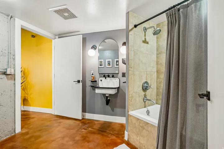 Bathroom featuring a wall-mounted sink, arched mirror with sconce lighting, and a bathtub with tiled surround