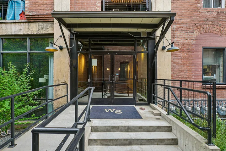 Building entrance featuring a glass door, metal awning, and concrete steps
