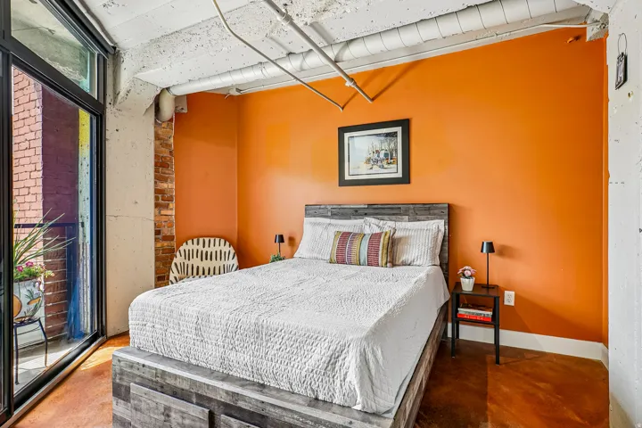 Bedroom featuring full-height glass doors opening to a private balcony, an exposed brick accent wall, concrete ceiling, and industrial-style exposed ductwork
