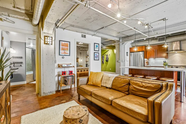 Open-concept living area featuring exposed ductwork, concrete ceilings, wood-finish flooring, a kitchen island with pendant lighting, and stainless steel appliances