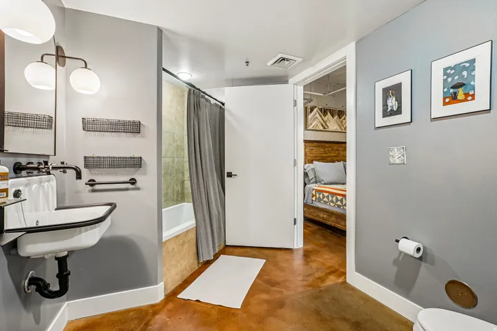 Bathroom featuring a wall-mounted sink with black fixtures and a mirror, complementing a tub/shower combination with tan tile surround