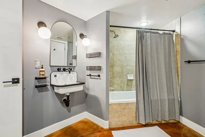 Bathroom featuring a unique wall-mounted sink, arched mirror with sconce lighting, and a tub-shower combination with tiled surround