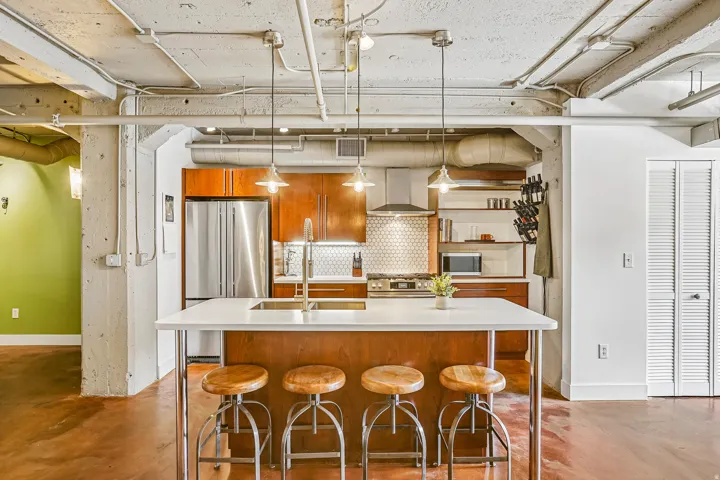 Modern kitchen featuring a central island with seating, stainless steel appliances, wood cabinetry, a tiled backsplash, and open shelving