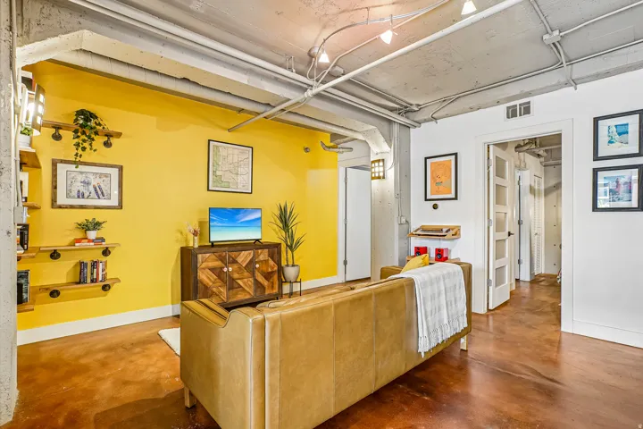 Exposed concrete ceiling with track lighting, industrial-style shelving, and a rich wood-finish floor
