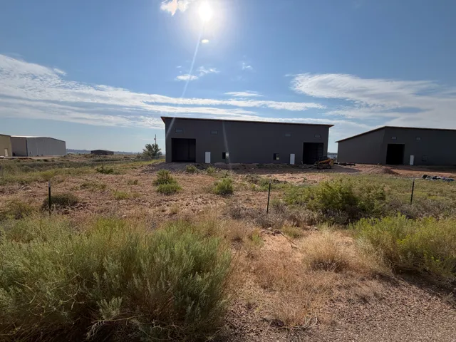 Two modern industrial buildings with dark gray siding and prominent entryways, situated on a large, undeveloped lot