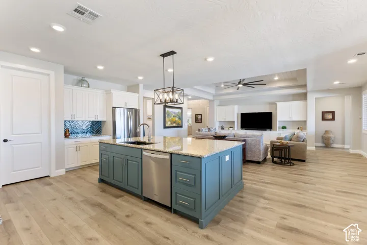 Spacious kitchen featuring a central island with a granite countertop, stainless steel appliances, and wood-finish flooring extending into the open living area with recessed lighting