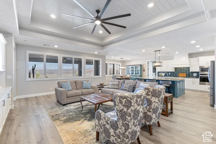 Spacious open-concept living area featuring wood-finish flooring, a tray ceiling with recessed lighting, and a large ceiling fan