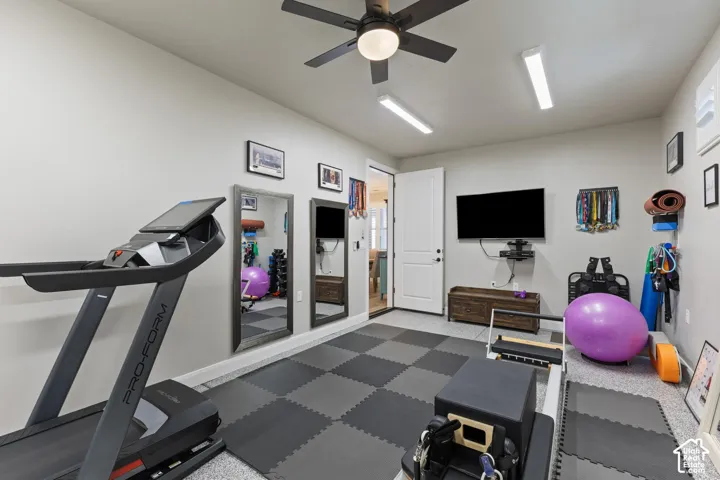 Dedicated fitness space featuring checkerboard-patterned flooring, a ceiling fan with integrated lighting, and multiple wall-mounted light fixtures