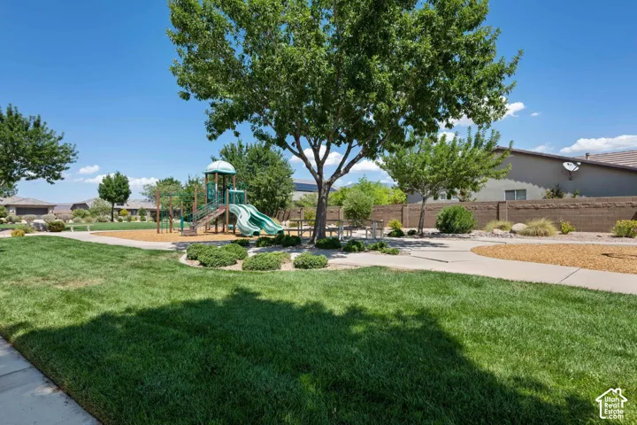 Community park featuring a green lawn, mature trees, a playground structure with slides, and paved walkways