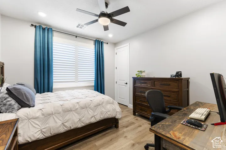 Bright interior room featuring a large window with plantation shutters, wood-finish flooring, recessed lighting, a ceiling fan, and a white interior door with dark hardware