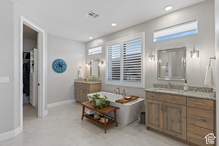 Bathroom featuring a freestanding tub, dual vanities with granite countertops, wood-finish cabinetry, and tiled flooring