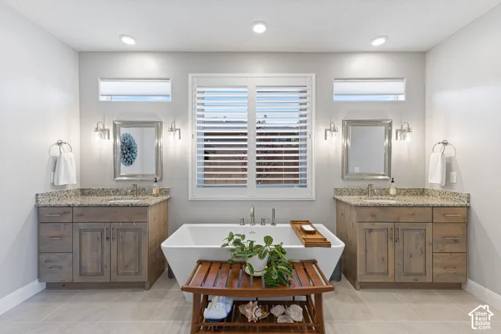 Freestanding soaking tub centered under a large window with white plantation shutters