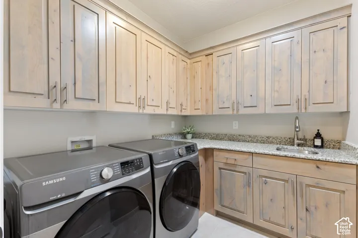 Laundry area featuring extensive light wood-finish cabinetry, granite-style countertops, an undermount sink with a gooseneck faucet, and light-toned walls