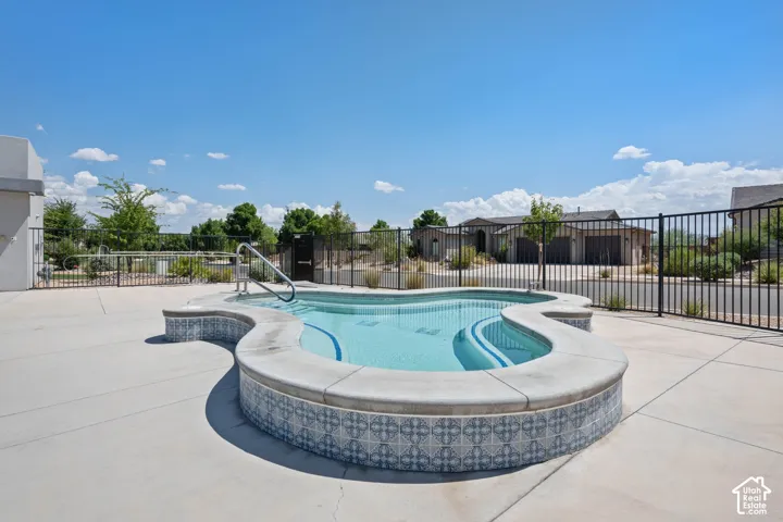 Curved pool with a light blue interior, patterned tile exterior, and a concrete deck