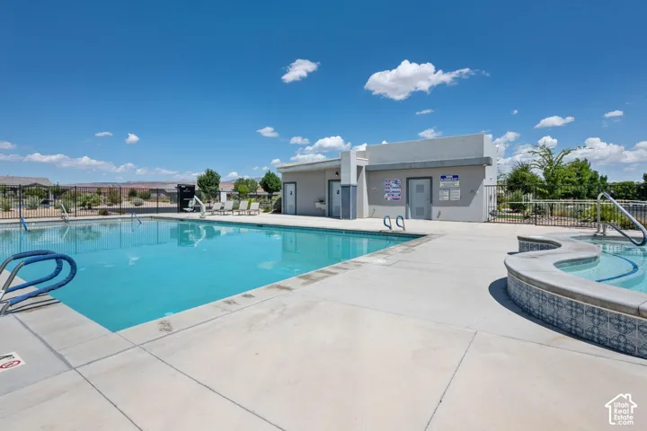 Outdoor swimming pool with concrete decking, an integrated spa with decorative tile, and a nearby building featuring access doors