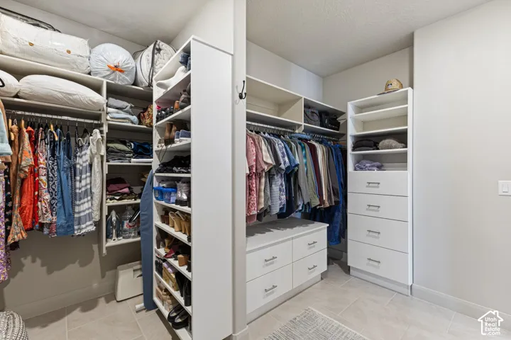 Spacious closet featuring custom built-in shelving, multiple hanging rods, integrated drawer storage, and light-toned tile flooring