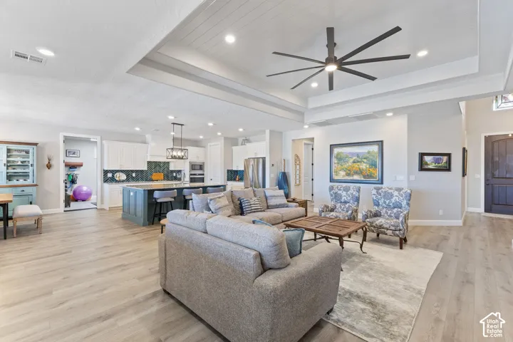 Expansive open-concept space featuring wood-finish flooring, a tray ceiling with a dark-blade ceiling fan, and recessed lighting