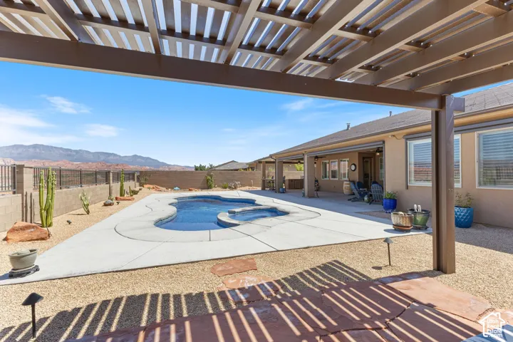 Rear patio featuring a pergola, a freeform swimming pool with integrated spa, concrete decking, and desert landscaping