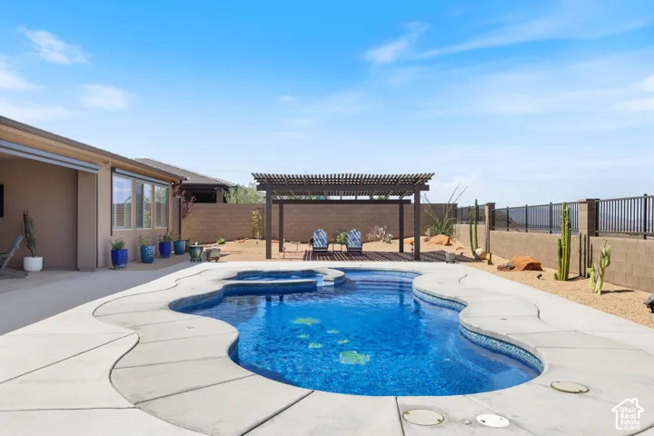Freeform swimming pool with integrated spa, concrete decking, a slatted pergola, and desert landscaping