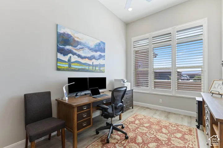 Office space featuring wood-finish flooring, white plantation shutters, and a ceiling fan