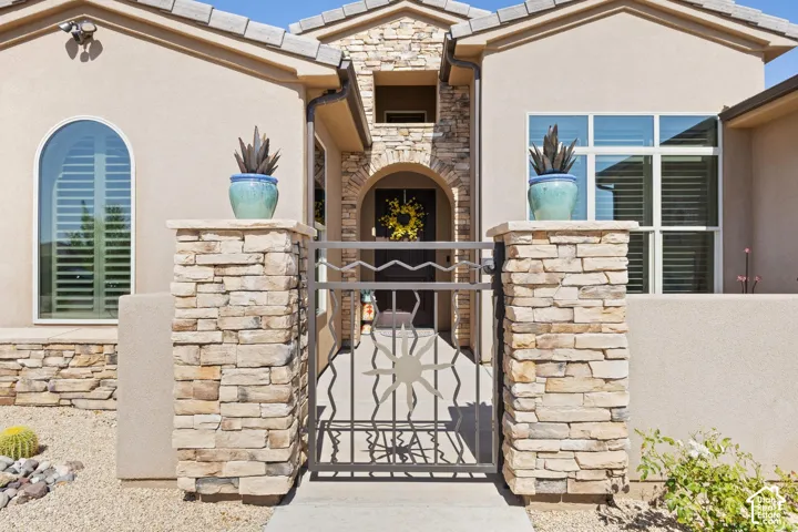 Stucco exterior with stone veneer accents, decorative wrought iron gate, arched entryway, and arched window with plantation shutters