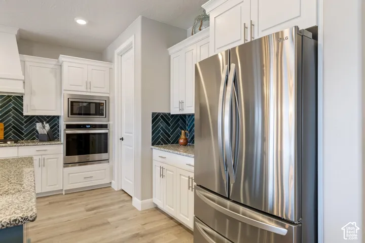 Contemporary kitchen featuring stainless steel appliances, white cabinetry, a dark herringbone tile backsplash, light wood-finish flooring, and light granite countertops