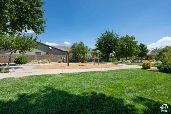 Community green space featuring a swing set, wood chip play area, concrete walking path, and mature trees