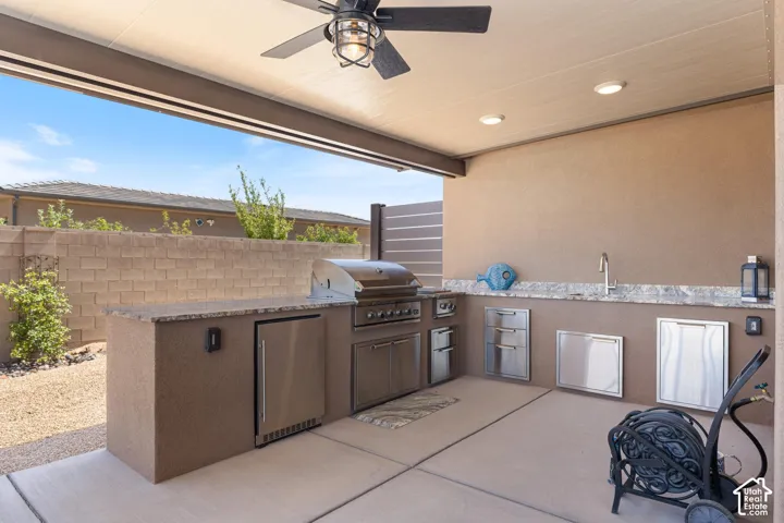 Covered outdoor kitchen featuring a built-in grill, integrated refrigerator, stainless steel sink, and ample counter space with a stone-finish backsplash
