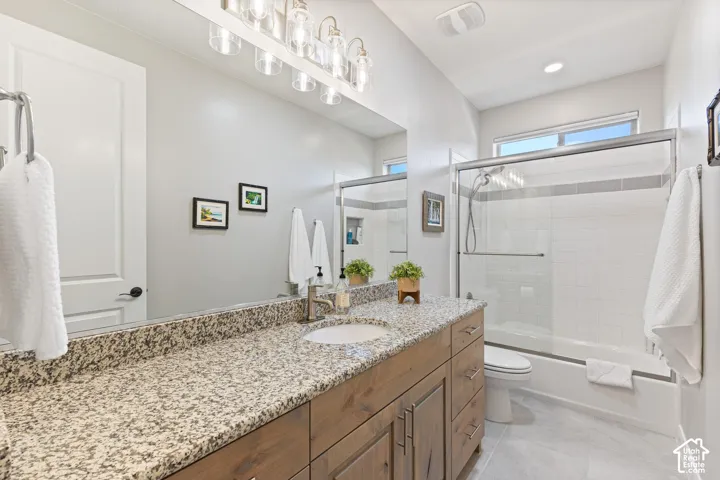 Bathroom featuring a spacious vanity with a speckled countertop, a large mirror, a light wood-finish vanity cabinet, a recessed sink, and a clear glass shower enclosure