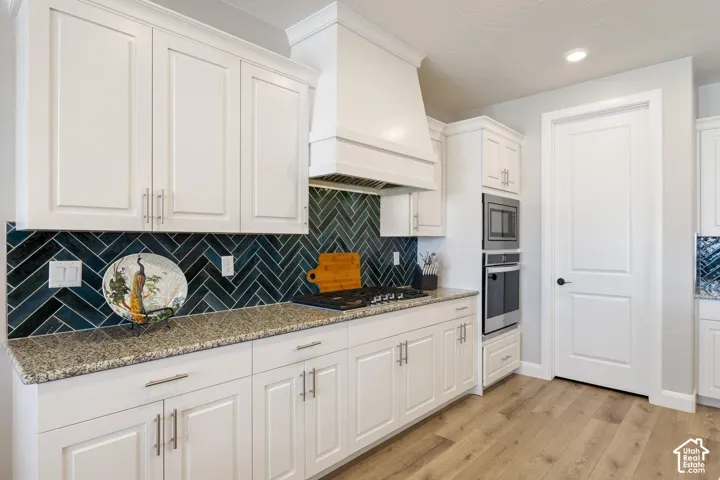 Kitchen featuring white shaker-style cabinetry, a dark herringbone tile backsplash, light speckled countertops, stainless steel appliances, and wood-finish flooring