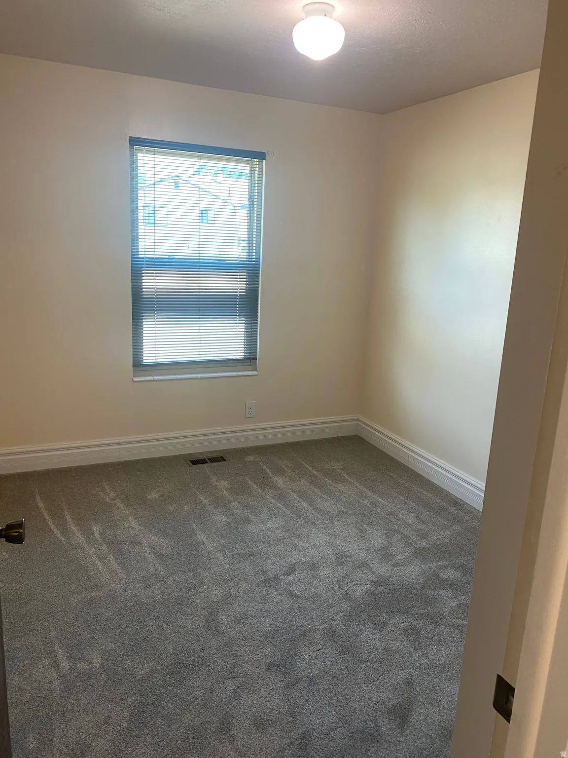Carpeted room featuring a single window with blinds, a ceiling-mounted light fixture, and white baseboards