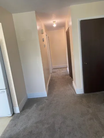 Hallway featuring neutral-toned walls, white baseboards, and wall-to-wall carpeting