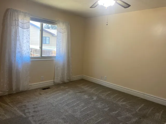 Carpeted room featuring a ceiling fan with integrated lighting, a window with white trim, and baseboard molding
