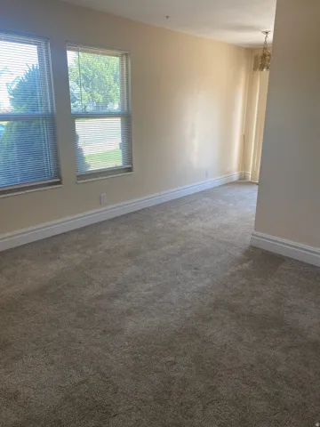 Bright room featuring neutral-toned carpet flooring, two windows with horizontal blinds, white baseboards, and a ceiling-mounted light fixture