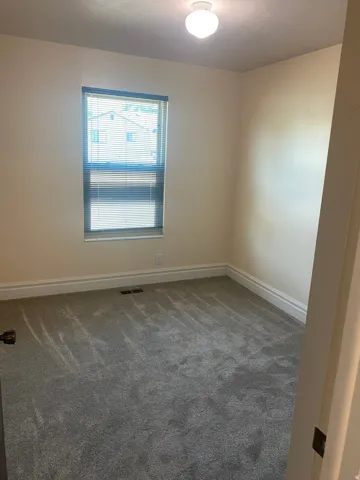 Carpeted room featuring a single window with blinds, a ceiling-mounted light fixture, and white baseboards