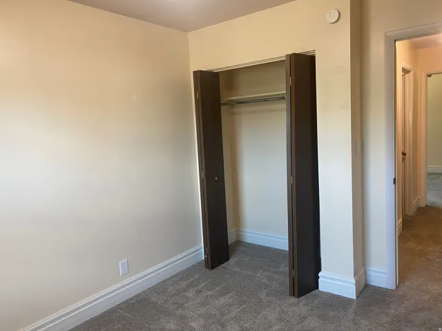 Carpeted interior room featuring a built-in closet with bifold doors, white baseboards, and neutral wall paint