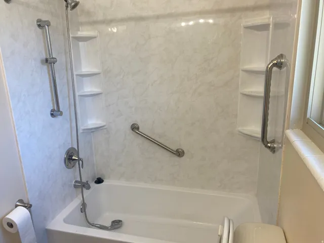 Tub and shower combination featuring a cultured marble surround, integrated shelving, and multiple grab bars