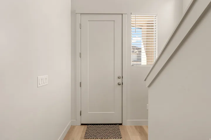 Entryway featuring a solid panel door, wood-finish flooring, and white walls