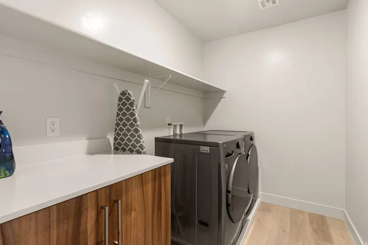 Laundry room featuring a built-in shelf, white countertops, wood-finish cabinetry with silver hardware, and light wood-finish flooring
