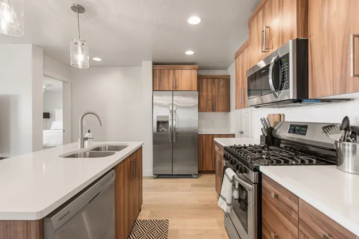 Contemporary kitchen featuring wood-finish cabinetry, stainless steel appliances, white countertops, and light wood-finish flooring