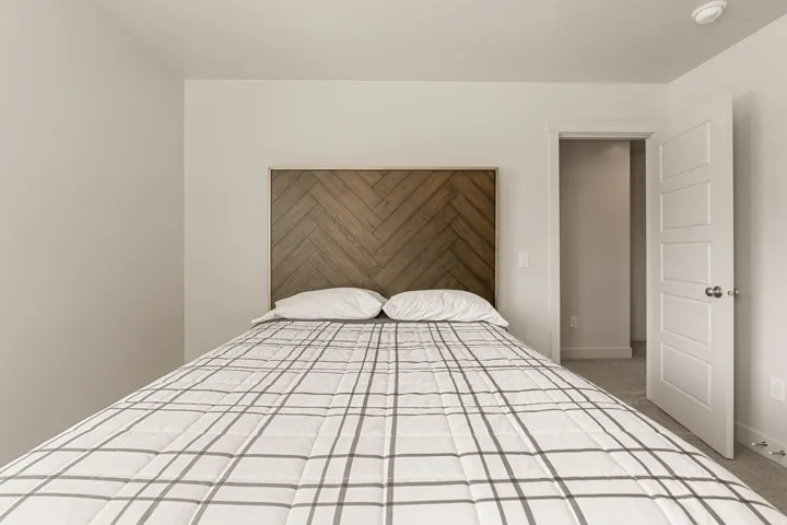 Bedroom featuring a built-in wood-finish headboard with a herringbone pattern, light neutral-toned walls, and carpet flooring