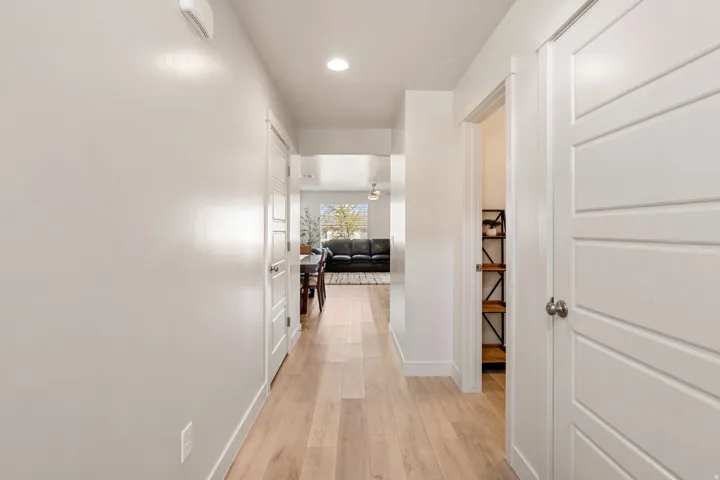 Hallway featuring light wood-finish flooring, white paneled doors, recessed lighting, and white baseboards