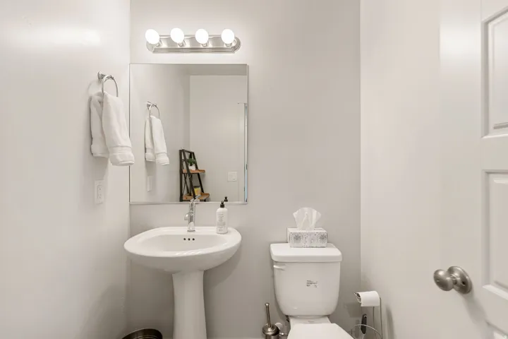 Compact bathroom featuring a pedestal sink, wall-mounted mirror, and a four-bulb vanity light fixture