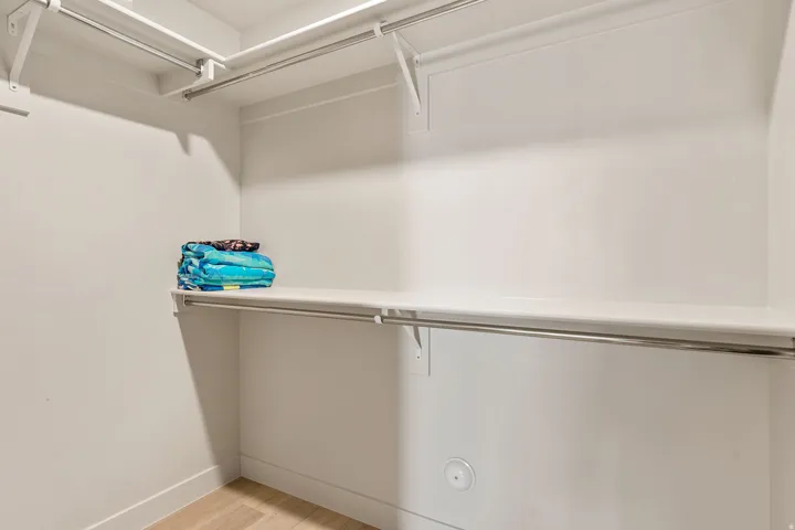 Walk-in closet featuring white walls, integrated shelving, and stainless steel clothing rods